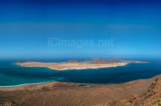 A sweeping panoramic view of La Graciosa, the smallest inhabited island of the Canary Islands, captured from the famous Mirador del Río viewpoint on Lanzarote. This photograph reveals the island’s golden sandy shores, turquoise waters, and rugged volcanic landscape, framed against the vast expanse of the Atlantic Ocean. This high vantage point offers a breathtaking perspective, showcasing the natural beauty and serene isolation of La Graciosa in stunning detail.
