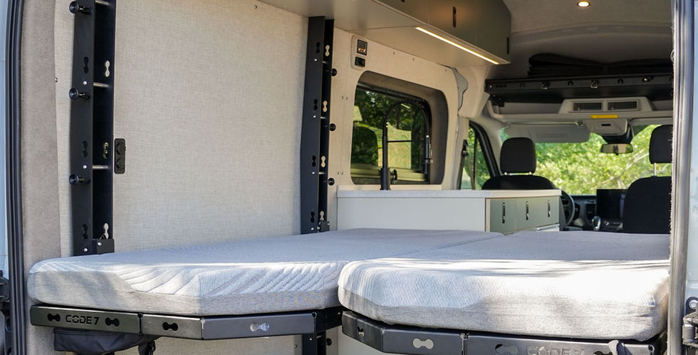 Voyager Ford Transit camper van rear interior with dual Code 7 bed platforms, open cargo space, queen size bed, overhead cabinets, warm LED lighting, and kitchen galley.