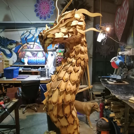 a dog standing next to a wooden dragon in a workshop