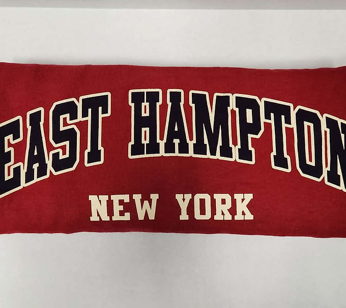 Red folded t shirt with "EAST HAMPTON NEW YORK" on it, displayed on white background.