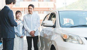 白い車の横に立つ夫婦に説明しているビジネスマン