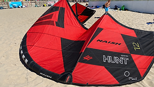 Een rood-zwarte Naish Hunt-kite van 12 m² staat opgepompt op het strand.