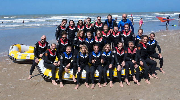 Groep deelnemers in wetsuits en zwemvesten poseert bij gele rafts op het strand van De Panne.