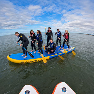 Bedrijfsteam peddelt en balanceert samen op een Mega SUP op zee in De Panne