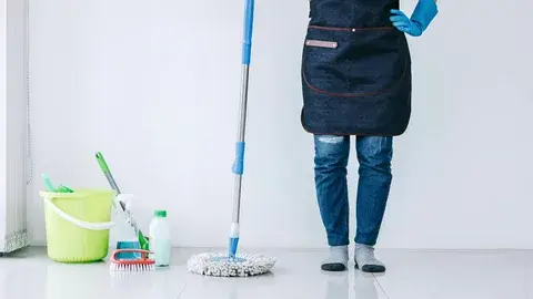 Person cleaning floor with mop and cleaning supplies nearby.