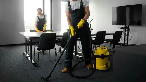 Workers cleaning an office with vacuum and table wipes.