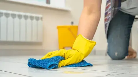 Person wearing gloves cleaning a tile floor with a cloth.