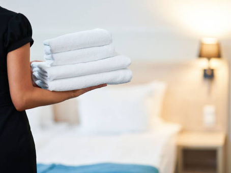 Housekeeper holding folded white towels in a hotel room.