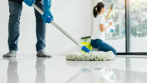 Workers cleaning a bright modern room with mop and cloth.