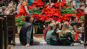 Children gather attentively amidst vibrant poinsettias, embodying the spirit of a festive holiday service.