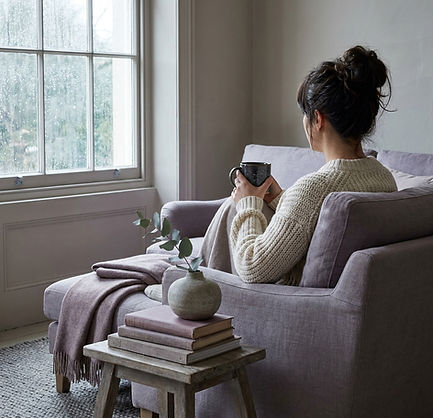 Woman in cream sweater sitting quietly by a window with tea, reflecting during 1:1 coaching for overachiever burnout