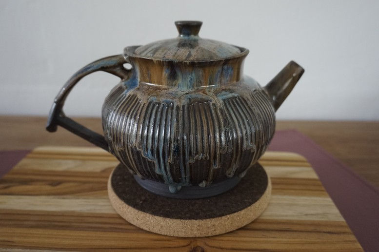 Thumbnail: Black ceramic teapot with a blue and gold glaze side view