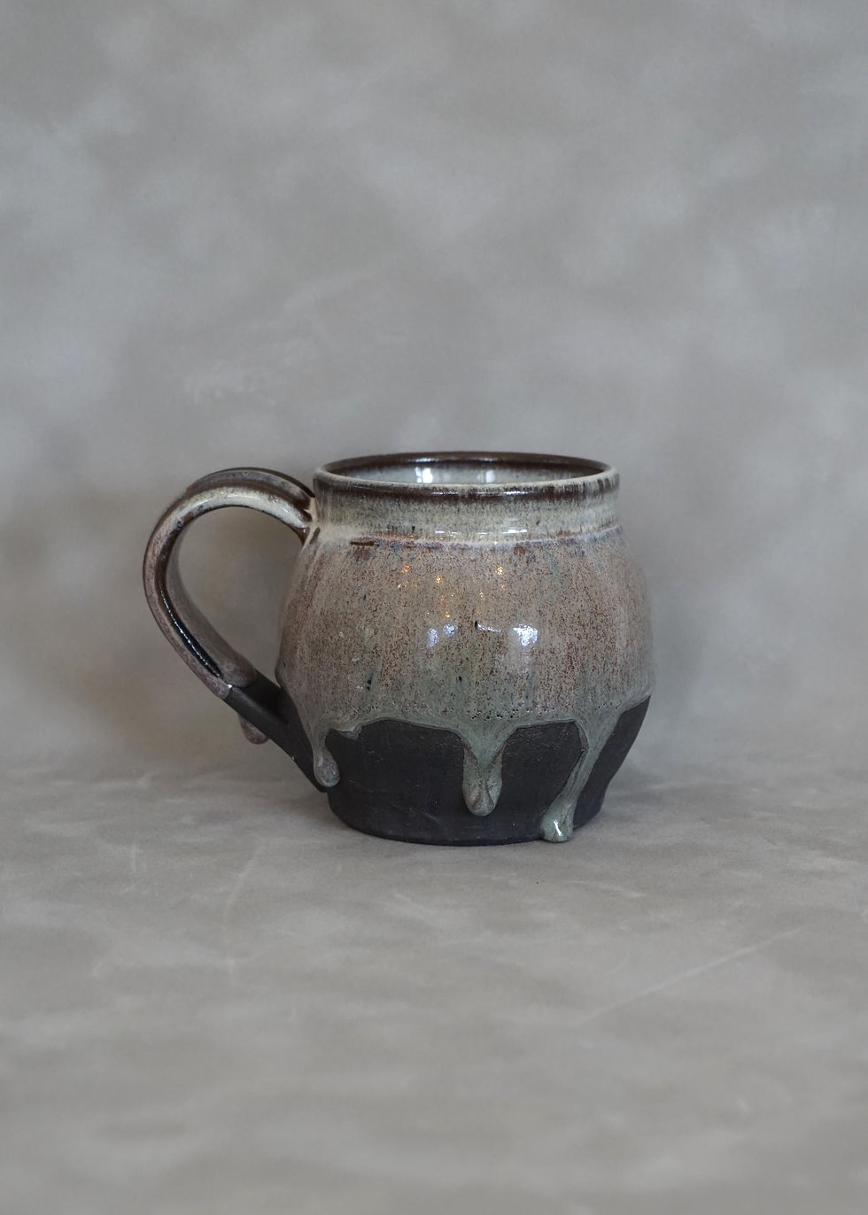 Thumbnail: Black clay globe mug with a white, red and green glaze side view