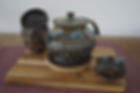 Black ceramic tea set with 4 cups and tea strainer with a blue and gold glaze side view