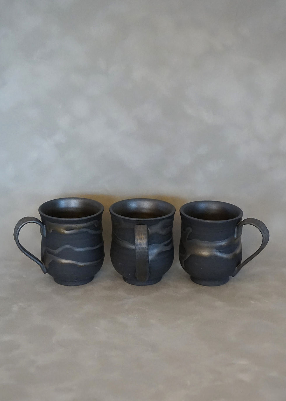 Thumbnail: 3 small espresso cups in black clay with a brassy glaze side view