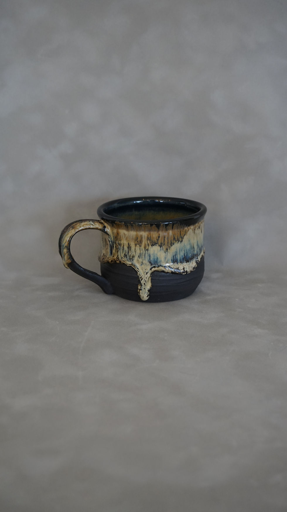 Thumbnail: Black clay ceramic mug with a beige glaze side view