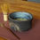 Thumbnail: Japanese-inspired tea bowl made from a grey clay with a textured black glaze and blue interior side view