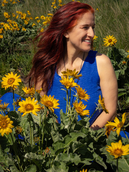 a woman in a blue tank top sits in a field of yellow flowers