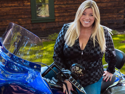 a woman in a checkered jacket sits on a blue motorcycle