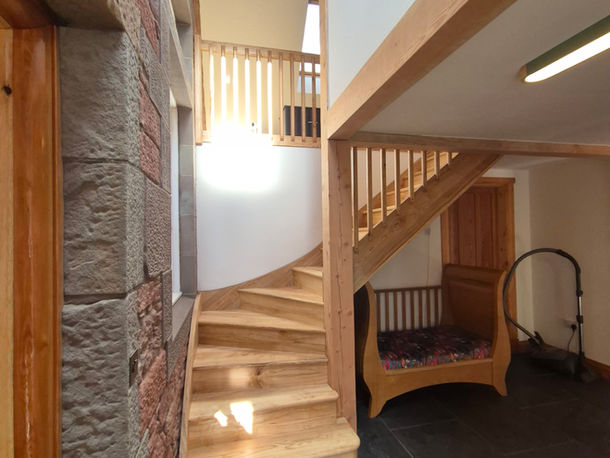 Bespoke curved oak staircase with wooden railings and stone wall detail in Scottish home.