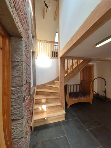 Handcrafted oak staircase with curved steps and railings, bespoke carpentry design in a traditional Scottish stone house.