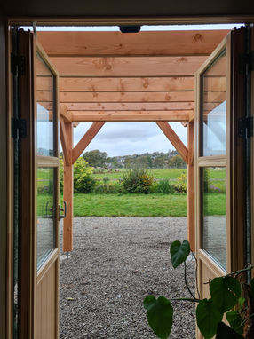 View through open double doors to a wooden pergola and garden beyond
