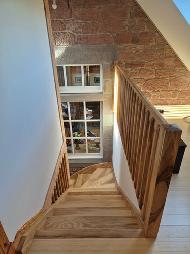 Handcrafted oak stairwell and railing with traditional joinery against exposed stone wall in a Scottish home