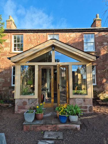 Bespoke oak framed porch extension with pitched roof, glass panels, and stone base on traditional home.