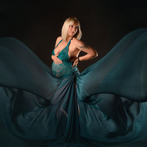 Femme blonde en robe verte, shootemotions 2023. Pose élégante devant fond sombre en studio.