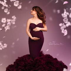 Femme enceinte élégante en robe bordeaux, posant parmi les fleurs flottantes.