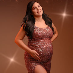 Femme enceinte souriante tenant son ventre, dans une robe pailletée.