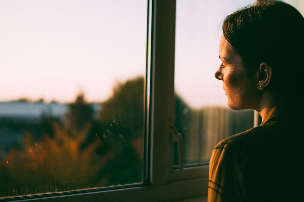 Image of women looking outside of a window as the sun shines on her face.