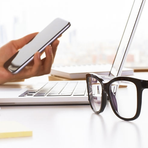 Closeup of business woman hands using cell phone and laptop on white desktop with glasses
