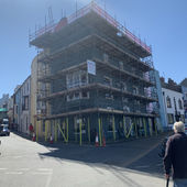 A sunny street with a corner building covered in scaffolding for renovation
