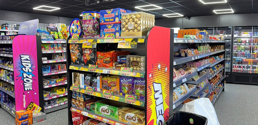 A brightly lit convenience store aisle displays colorful candy and snack shelves