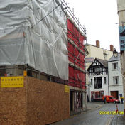 Street with a construction site on the left, covered in plastic and red netting