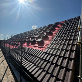 Brown roof tiles partially installed on a roof against a clear blue sky