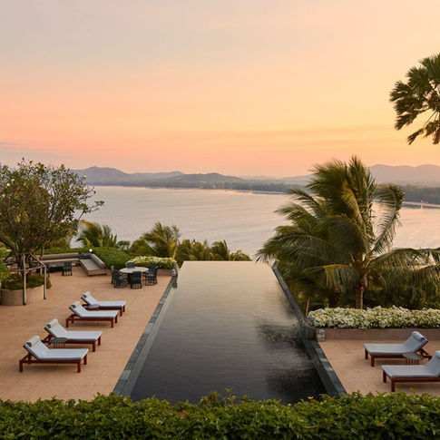 Infinity pool overlooking a serene ocean at sunset, surrounded by palm trees and lounge chairs