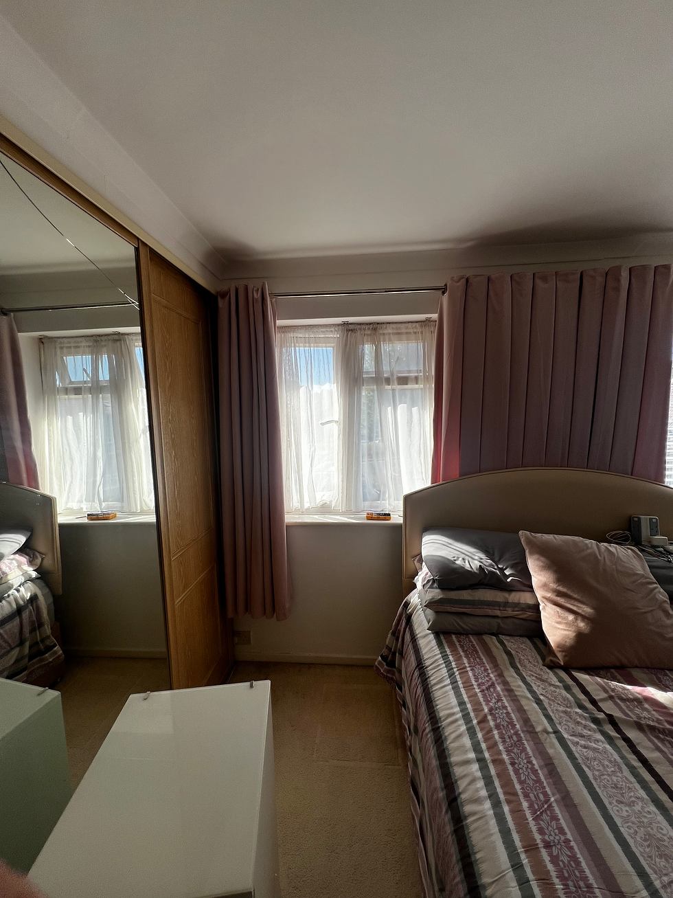 Bedroom with pink curtains framing a window beside a mirrored wardrobe and double bed