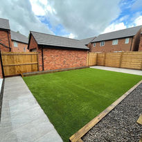 A well-maintained backyard with lush green grass, bordered by a wooden fence and red brick walls