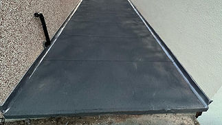 Newly paved black concrete path with side rail flanked by rough-textured and smooth walls
