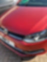 Close-up of a red Volkswagen car's front, highlighting one headlight and the VW logo