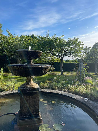 A two-tiered stone fountain sprays water in a sunlit garden
