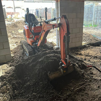 An orange Kubota mini digger parked on a large mound of soil inside a property extension