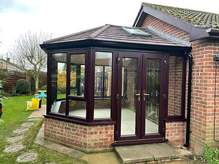 A brick house with a modern conservatory extension featuring large glass windows and doors