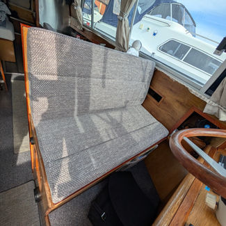 Boat interior showing a gray cushioned seat by a wooden steering wheel