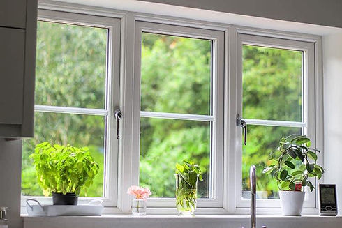 Three potted plants and a small vase with pink flowers sit on a bright windowsill