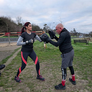 A woman and a man practice boxing outdoors on a grassy area
