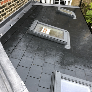 A wet, dark slate roof with three rectangular skylights