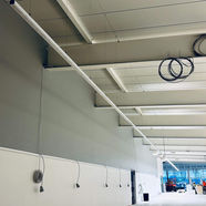 An interior view of a spacious room with a high ceiling featuring installed lighting fixtures and electrical wires hanging from the ceiling